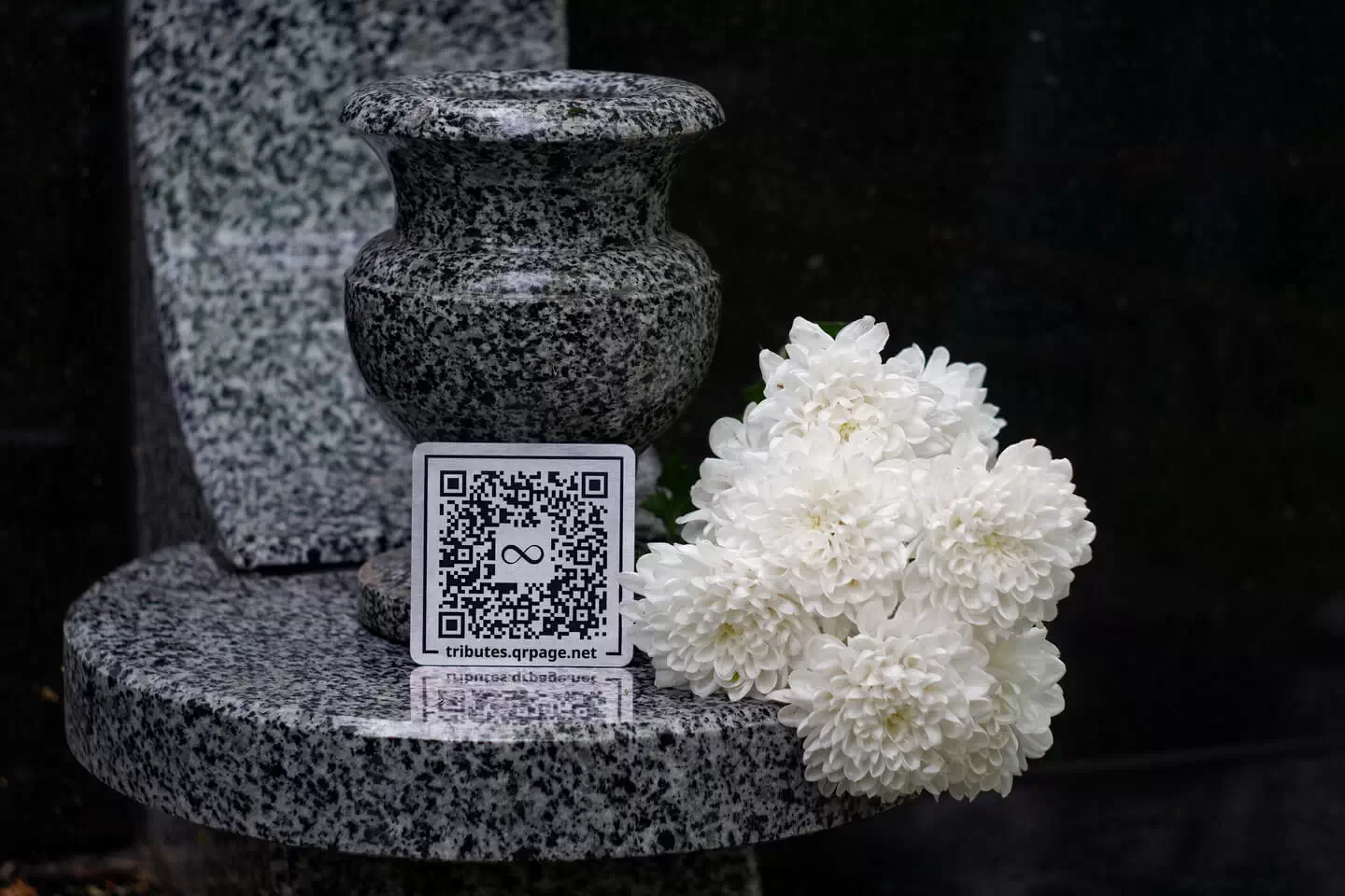 Гранітна урна з білими квітами та QR-кодом на меморіальному постаменті